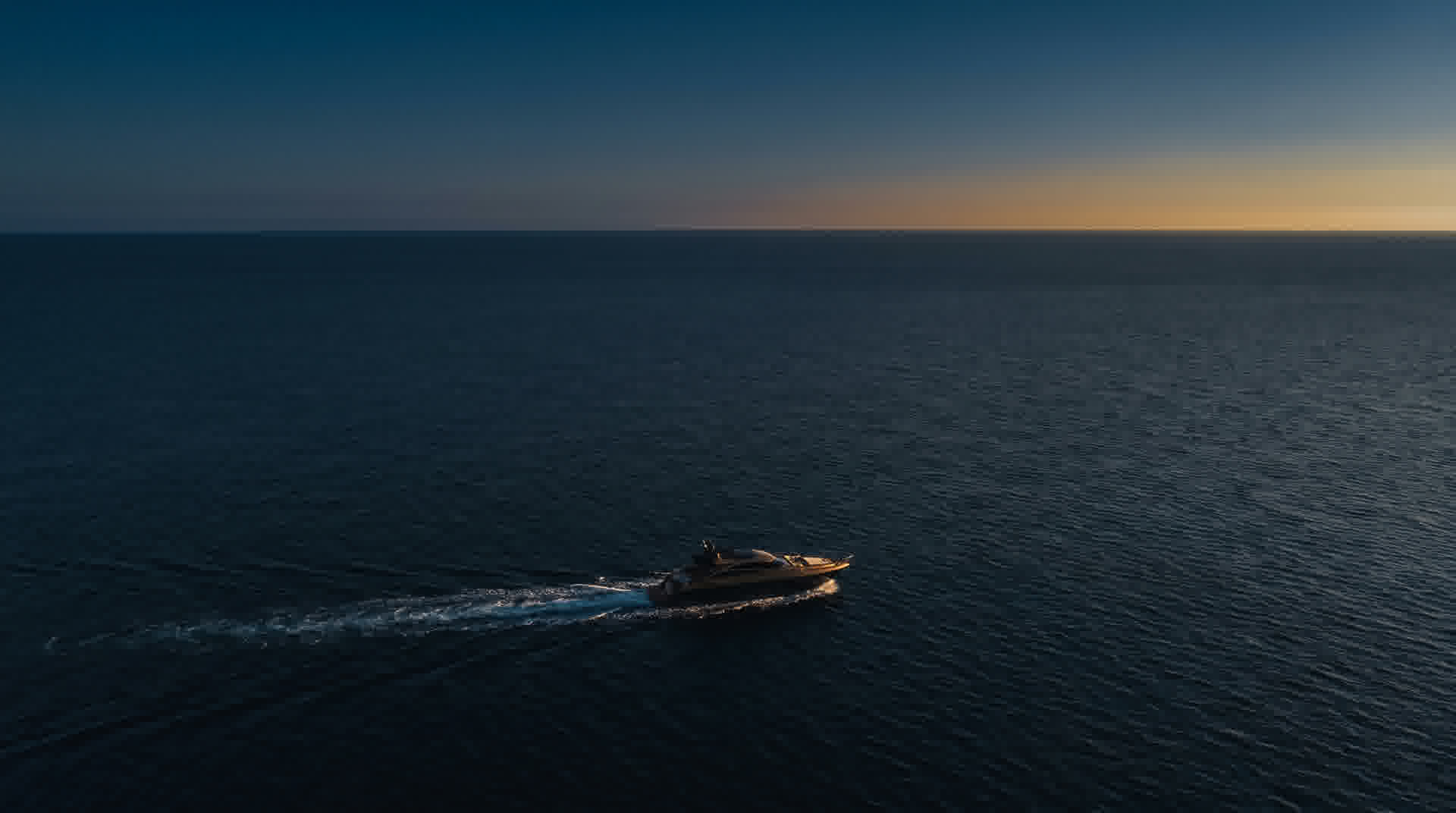 A private yacht crossing calm navy waters at dusk, golden light on the horizon